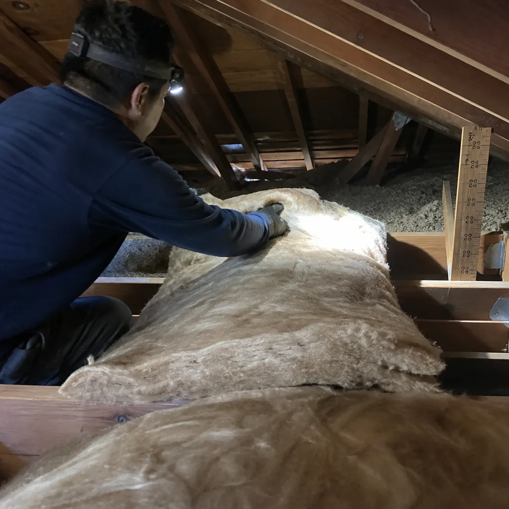 Technician installing fiberglass attic insulation in a wooden roof structure